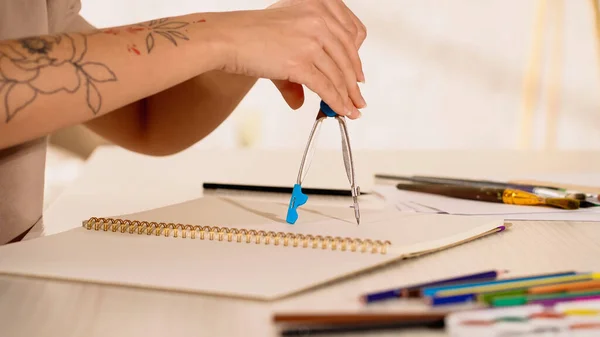 Partial view of tattooed woman drawing with compass on sketchbook at home — Stock Photo