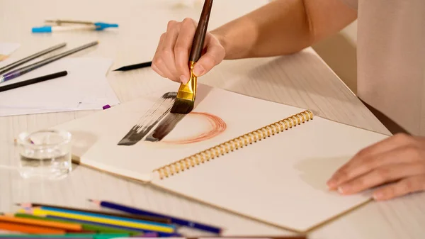 Vue recadrée de la peinture femme sur carnet de croquis près des crayons de couleur flous et du papier — Photo de stock