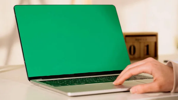 Vue recadrée de femme floue à l'aide d'un ordinateur portable avec écran vert à la maison — Photo de stock