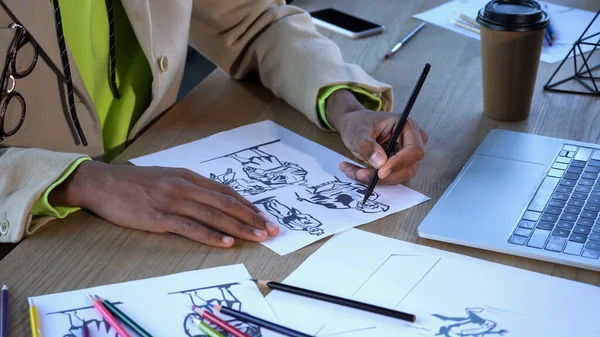 Cropped view of african american designer drawing sketches near devices and paper cup in studio — Stock Photo
