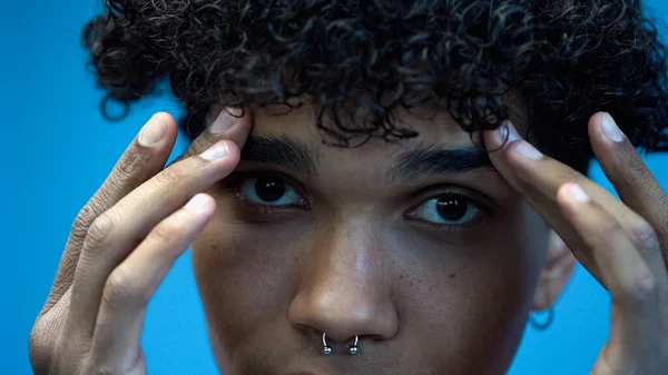 Cropped view of young african american man touching eyebrows isolated on blue — Stock Photo