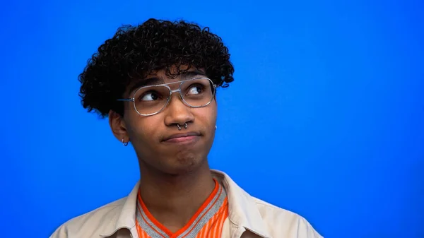 Pensativo joven afroamericano hombre en gafas mirando hacia otro lado aislado en azul - foto de stock