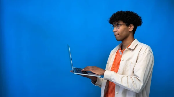 Pensativo freelancer afroamericano en gafas usando portátil sobre fondo azul - foto de stock