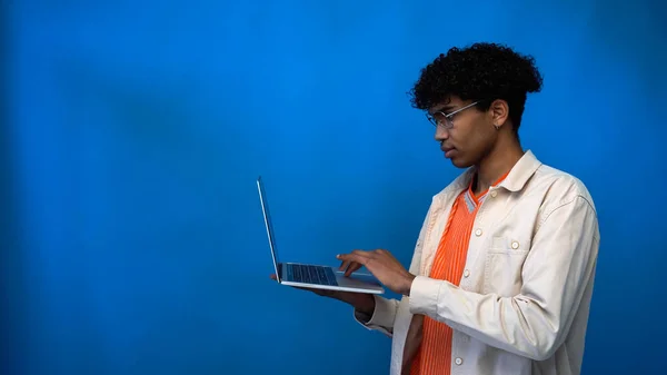 Young african american man in eyeglasses using laptop on blue background with copy space — Stock Photo