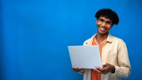 Freelancer afro-americano feliz em óculos segurando laptop isolado em azul — Fotografia de Stock