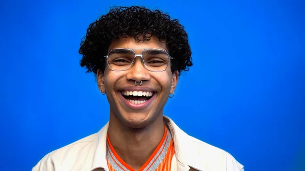 Веселий афроамериканець у окулярах сміється ізольовано на синьому — стокове фото