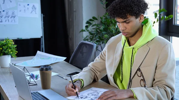 Le designer afro-américain dessine des croquis près des appareils et du café pour aller en studio — Photo de stock