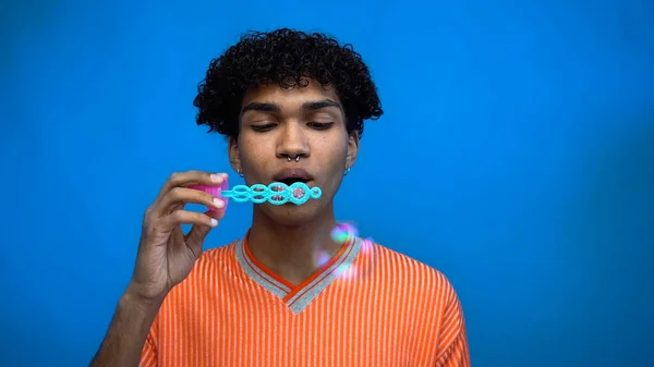 Young african american man blowing soap bubbles isolated on blue — Stock Photo