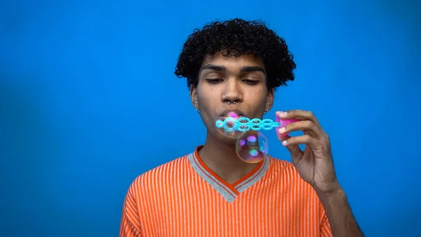 Elegante afroamericano hombre soplando burbujas de jabón aislado en azul - foto de stock