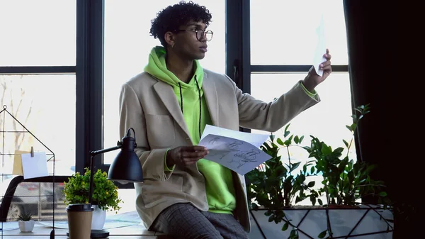 Elegante designer afro-americano olhando para esboços em estúdio — Stock Photo