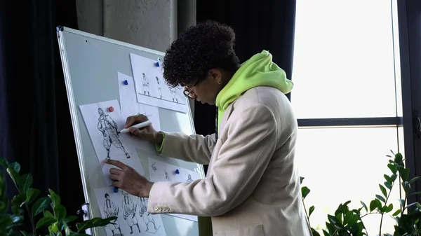 Side view of african american designer drawing sketches on flip chart in studio — Stock Photo