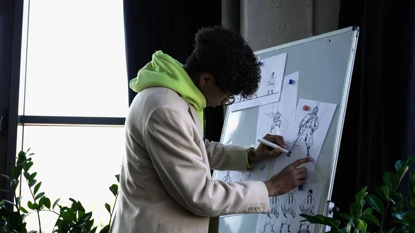 Elegante designer afro-americano desenhando esboços em estúdio — Fotografia de Stock