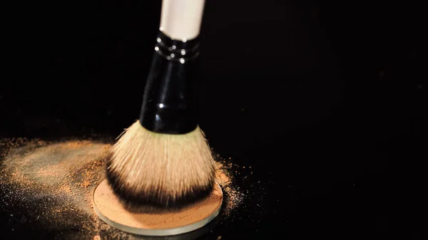 Vista de cerca del cepillo cosmético borroso y el polvo facial sobre fondo negro - foto de stock