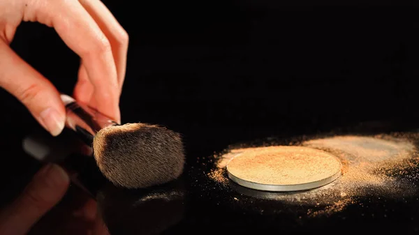 Cropped view of woman holding cosmetic brush near face powder on black surface — Stock Photo