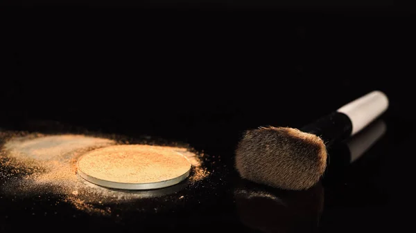Spazzola cosmetica vicino alla polvere beige su superficie nera — Foto stock
