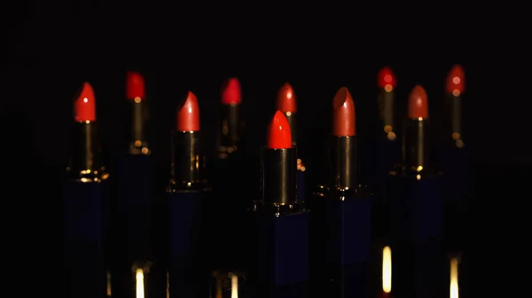 Vista de cerca de los lápices labiales rojos con desenfoque sobre fondo negro - foto de stock