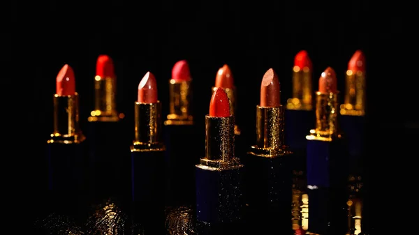 Diferentes tonos de lápices labiales rojos en la superficie negra húmeda - foto de stock