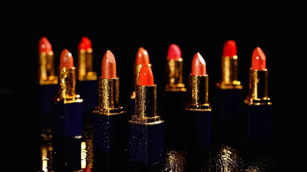 Wassertropfen in verschiedenen Schattierungen roter Lippenstifte auf schwarzem Hintergrund — Stockfoto