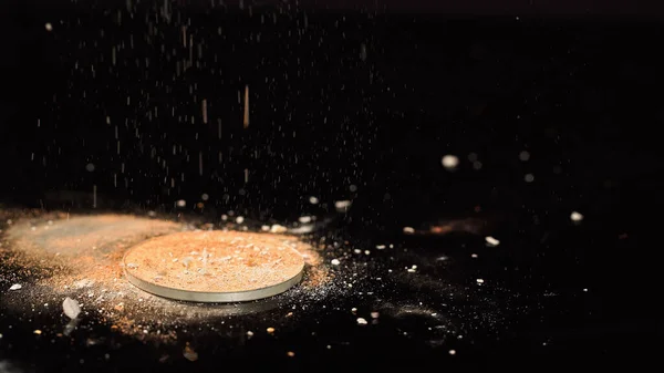 Close up view of beige face powder pouring on black background — Stock Photo