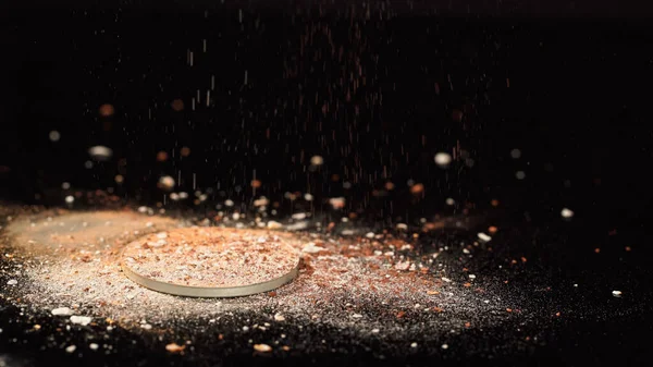 Crushed beige face powder on blurred black background — Stock Photo