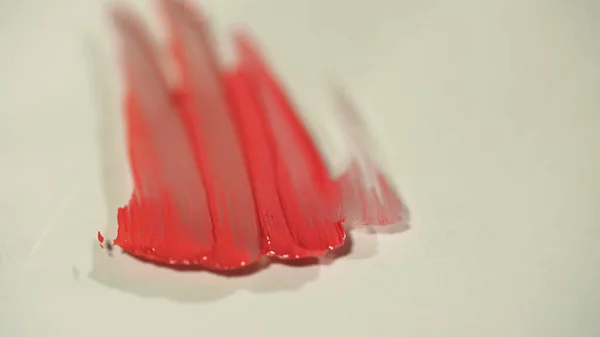 Visão aproximada de traços de brilho labial vermelho na superfície cinza — Fotografia de Stock
