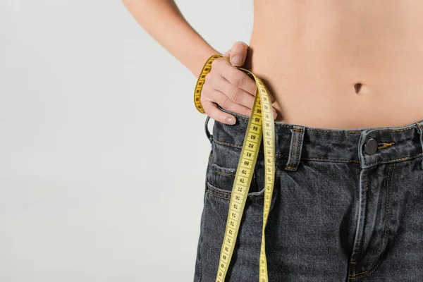 Partial view of slender woman standing with hand on hip and holding measuring tape isolated on grey — Stock Photo