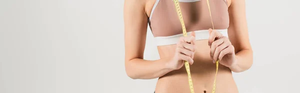 Partial view of woman in sports top holding measuring tape isolated on grey, banner — Stock Photo