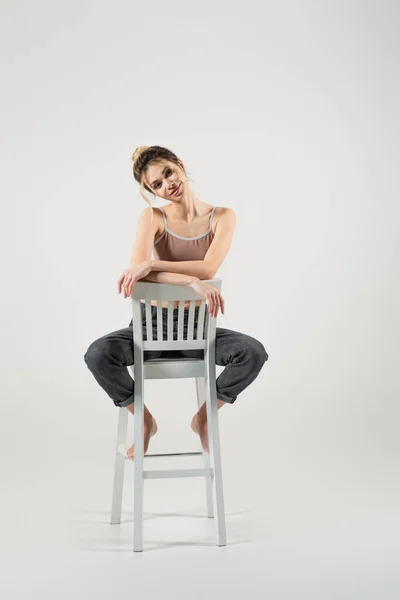 Cheerful and fit woman looking at camera while posing on chair on grey background — Stock Photo