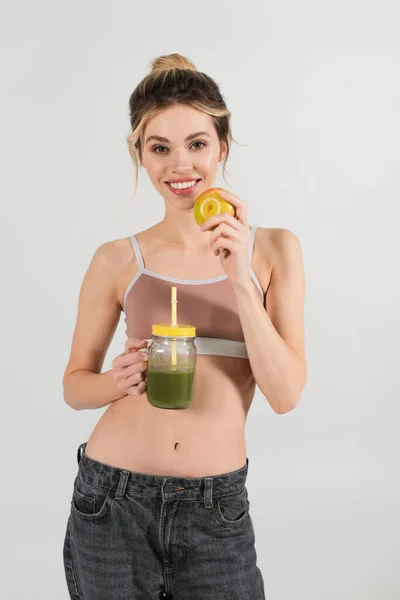 Young woman with perfect face and body holding ripe apple and fresh smoothie isolated on grey — Stock Photo