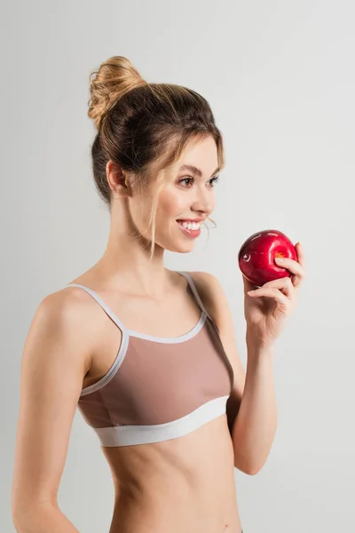 Femme en forme gaie avec maquillage naturel et pomme fraîche regardant loin isolé sur gris — Photo de stock