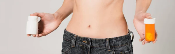 Vista parziale di donna in forma in jeans con vitamine in contenitori isolati su grigio, banner — Foto stock