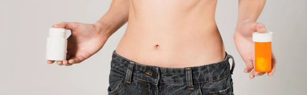 Vista parcial de la mujer en forma en jeans con vitaminas en recipientes aislados en gris, pancarta - foto de stock