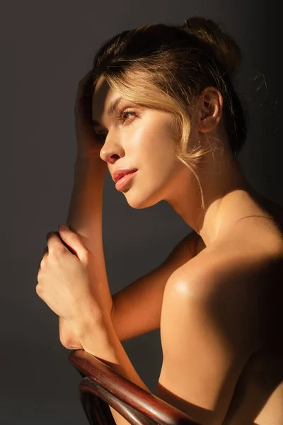Nackte Frau mit perfekter Haut und natürlichem Make-up sitzt in Licht isoliert auf grau — Stockfoto