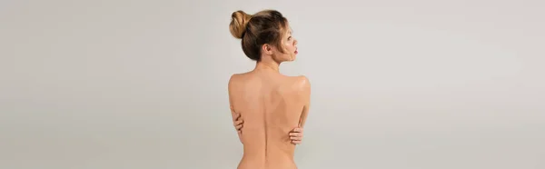 Vista posteriore della donna nuda che si abbraccia mentre posa isolata sul grigio, striscione — Foto stock