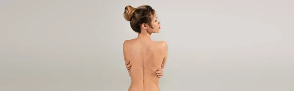 Back view de mulher nua abraçando-se enquanto posando isolado em cinza, banner — Fotografia de Stock