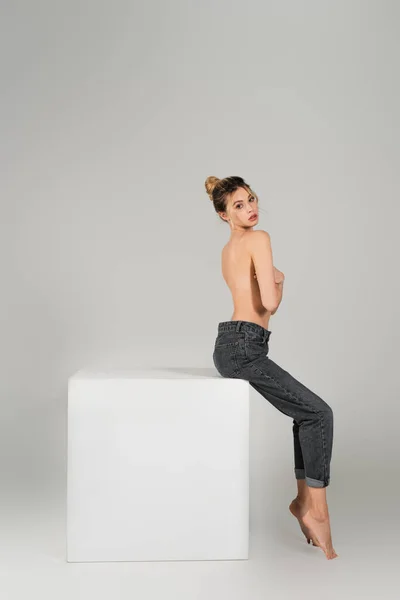 Sensual mujer semidesnuda con cuerpo perfecto sentado en jeans en silla blanca sobre fondo gris — Stock Photo