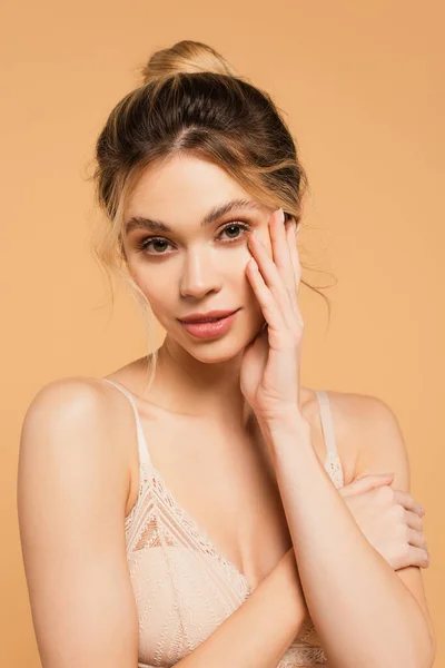 Retrato de mujer encantadora en sujetador agarrado de la mano cerca de la cara con maquillaje natural aislado en beige - foto de stock