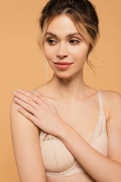 Positive woman in bra touching perfect skin and looking away isolated on beige — Stock Photo