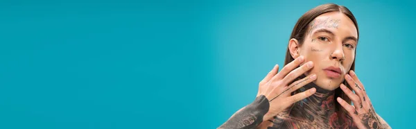 Молодий чоловік з татуюваннями торкається гладкого обличчя ізольовано на синьому, банер — Stock Photo