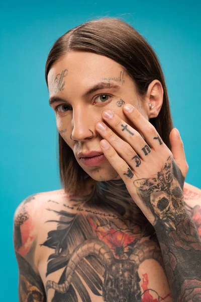 Young man with tattoos applying cream under eye isolated on blue — Stock Photo