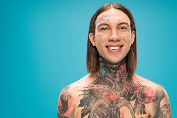 Cheerful young man with tattoos smiling and looking at camera isolated on blue — Stock Photo