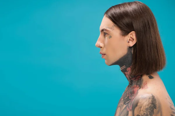 Side view of young and pierced man with tattoos looking away isolated on blue — Stock Photo