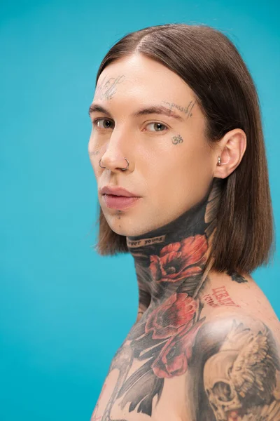 Young and pierced man with tattoos looking at camera isolated on blue — Stock Photo