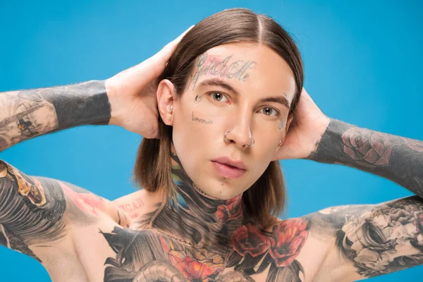 Jeune homme percé avec des tatouages regardant la caméra tout en posant isolé sur bleu — Photo de stock