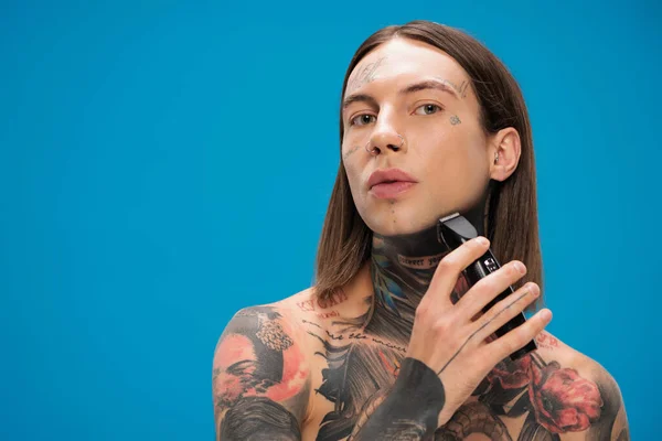 Jeune homme percé avec des tatouages rasage avec rasoir électrique isolé sur bleu — Photo de stock