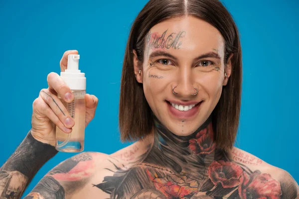 Homem feliz e tatuado segurando garrafa com espuma de limpeza isolado em azul — Fotografia de Stock