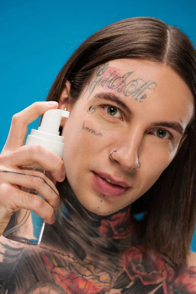 Hombre joven y perforado sosteniendo la botella con espuma limpiadora aislada en azul - foto de stock