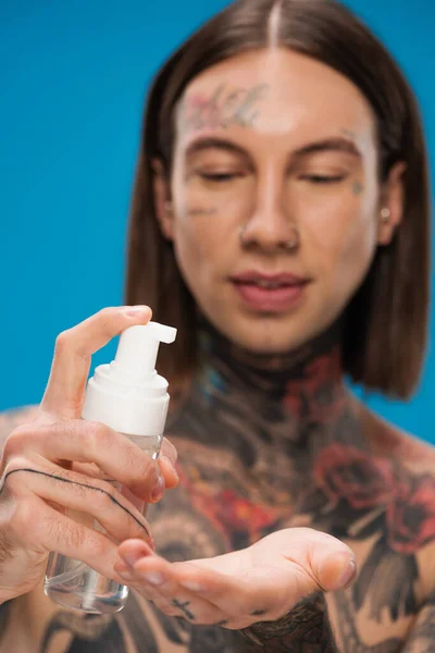 Homem desfocado e tatuado segurando garrafa com espuma de limpeza isolado em azul — Fotografia de Stock