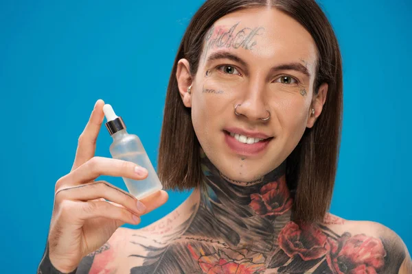 Hombre feliz y tatuado sosteniendo botella con suero aislado en azul - foto de stock