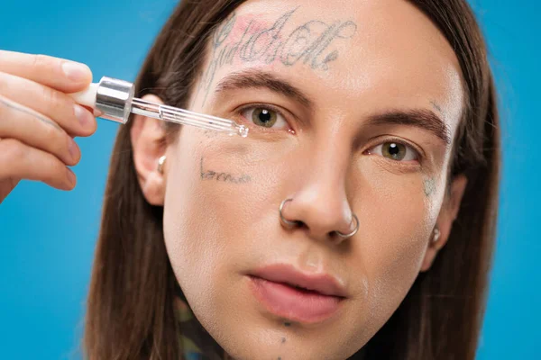 Close up of young and tattooed man applying moisturizing serum isolated on blue — Stock Photo